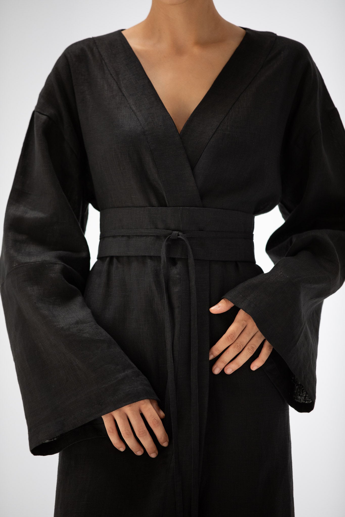 a close up of a black kimono made of pure linendesigned by atelier mizuni, worn by a person on a white background.