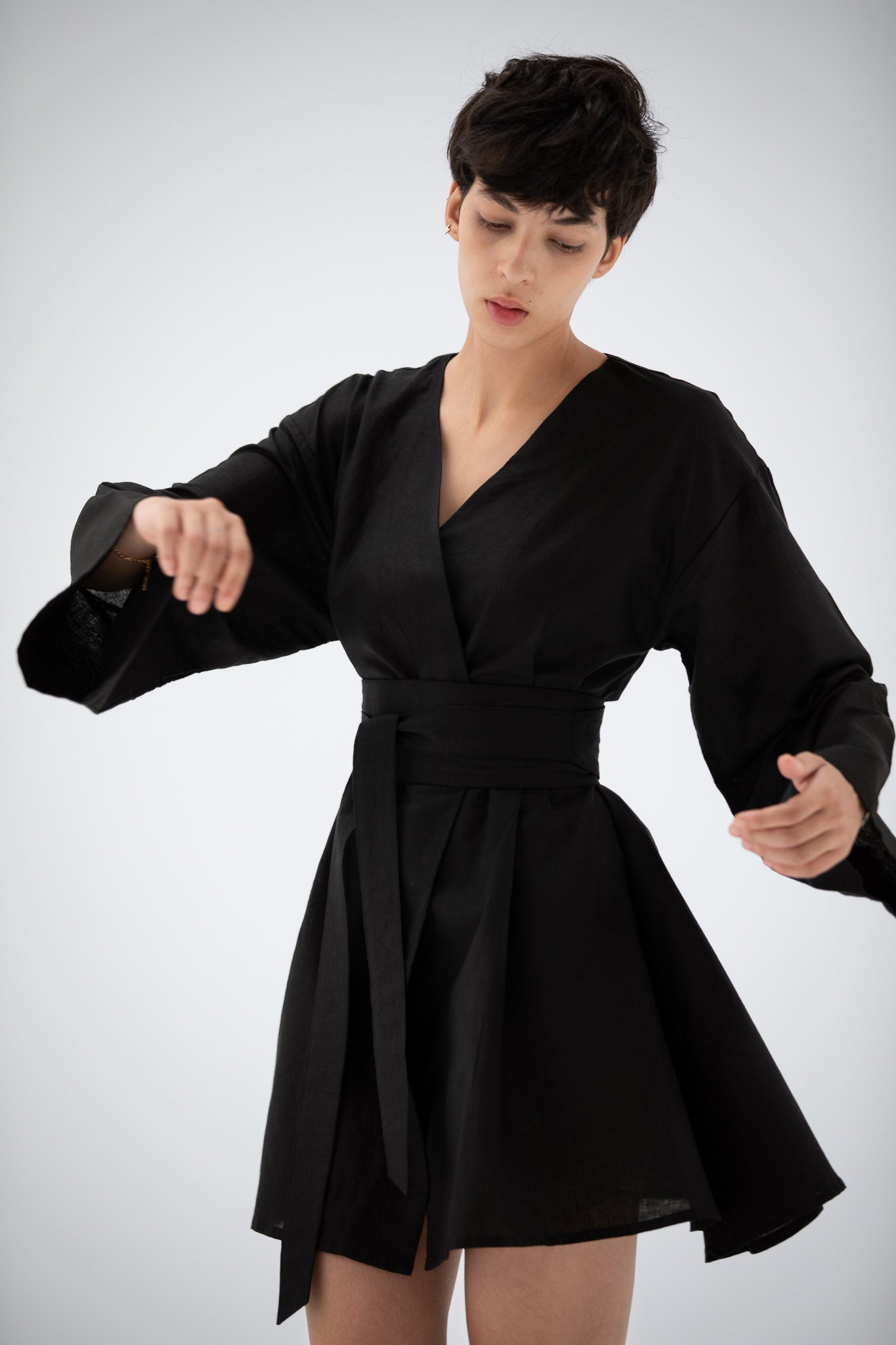 Woman wearing a black short kimono dress made of linen with a white background