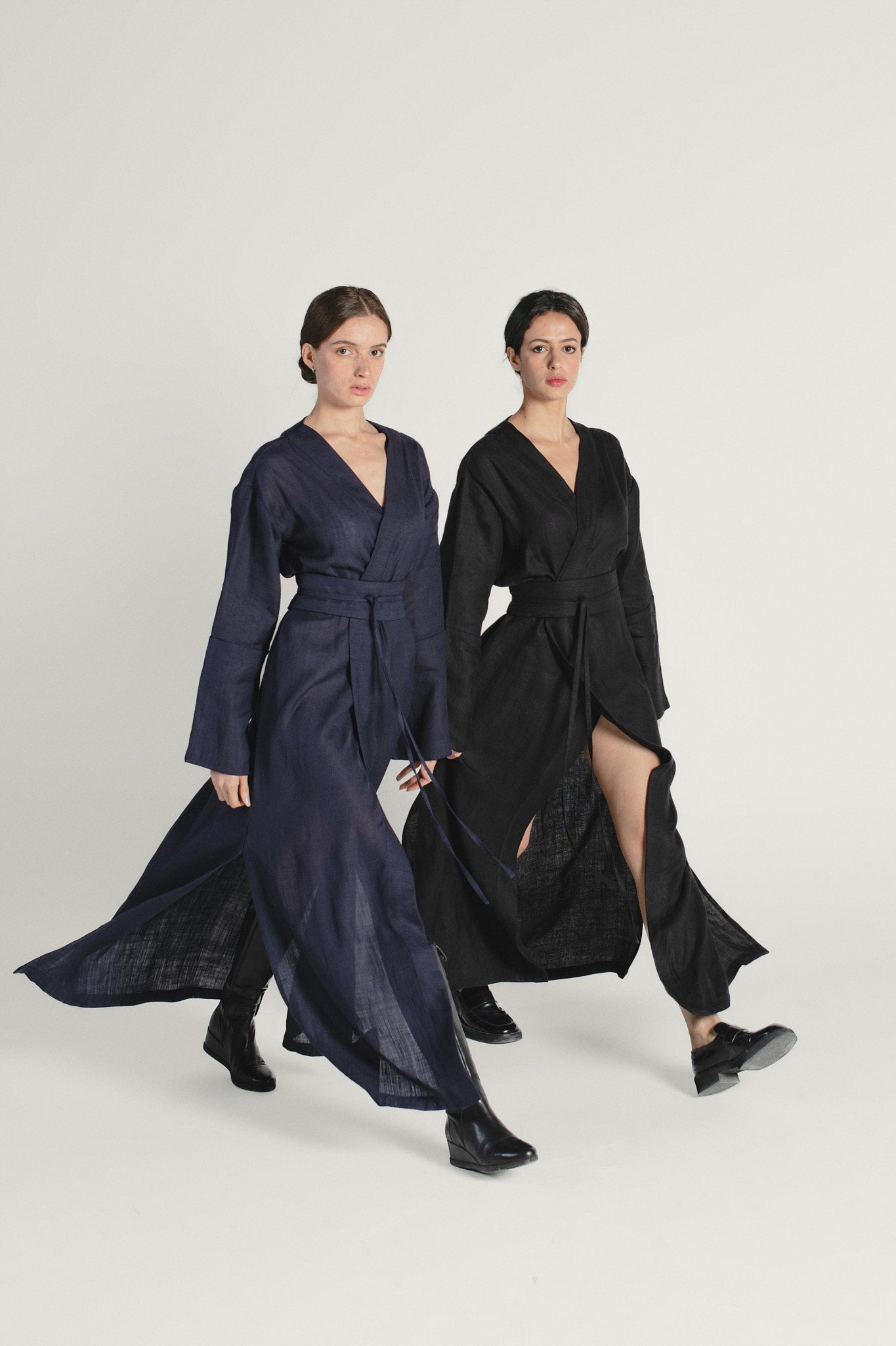 Two models cat walking and looking at the camera. One wearing a black linen kimono dress and another one wearin a midnight Blue linen kimono dress made by atelier mizuni