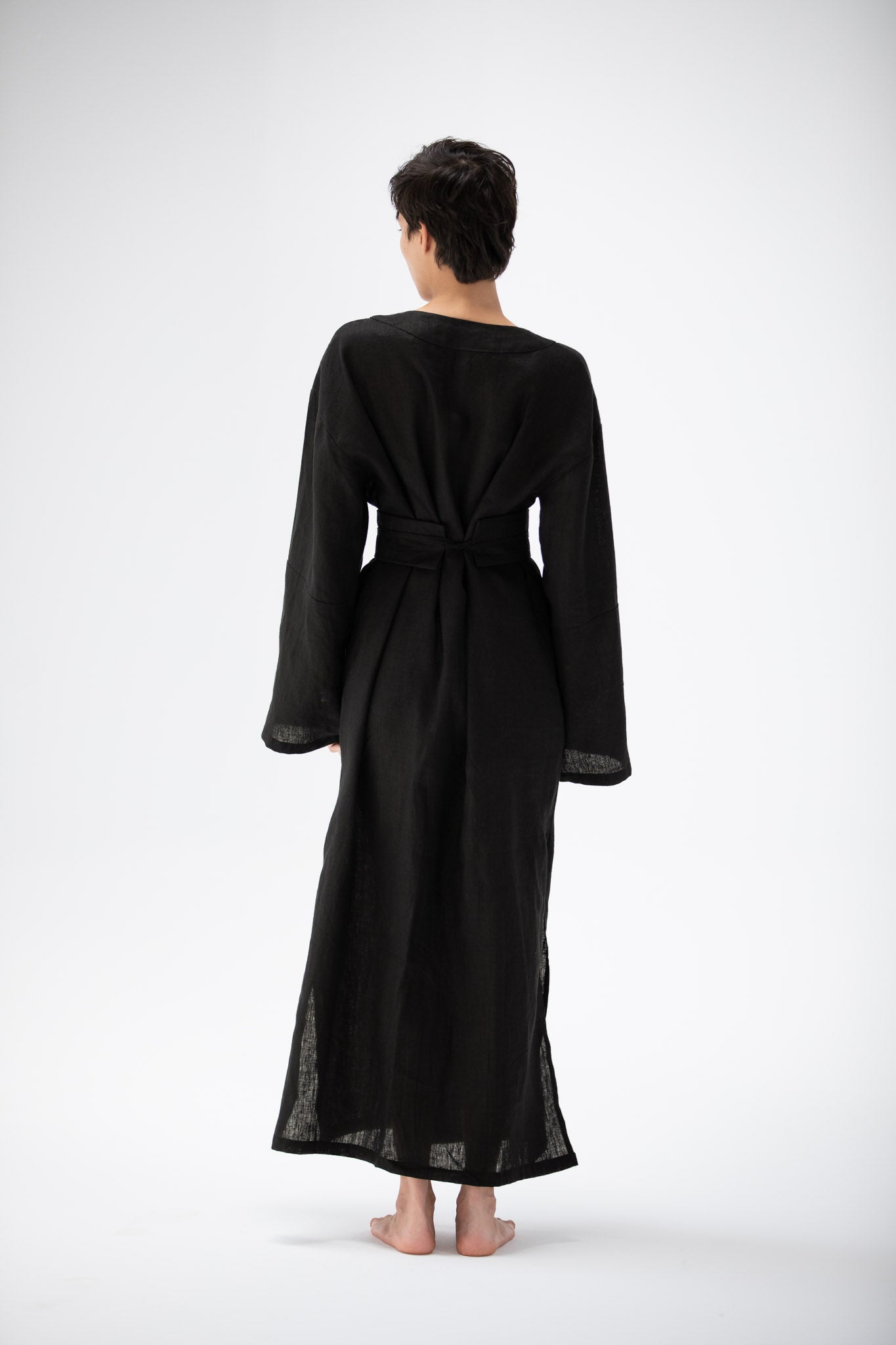 Person wearing a black long-sleeve kimono inspired dress with an obi belt on a white background.