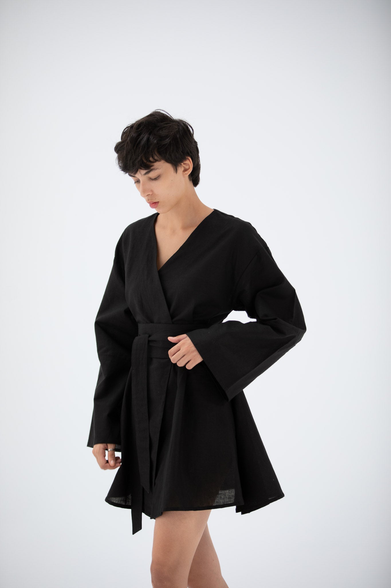Woman wearing a black short kimono dress made of linen with wide sleeves on a white background.