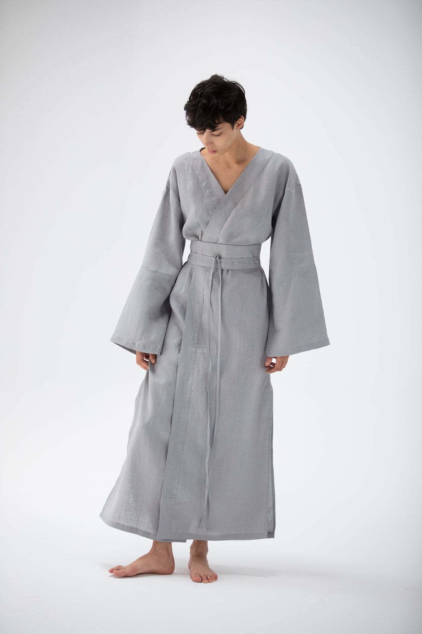 Person wearing a gray blue kimono inspired dress designed by atelier mizuni on a white background