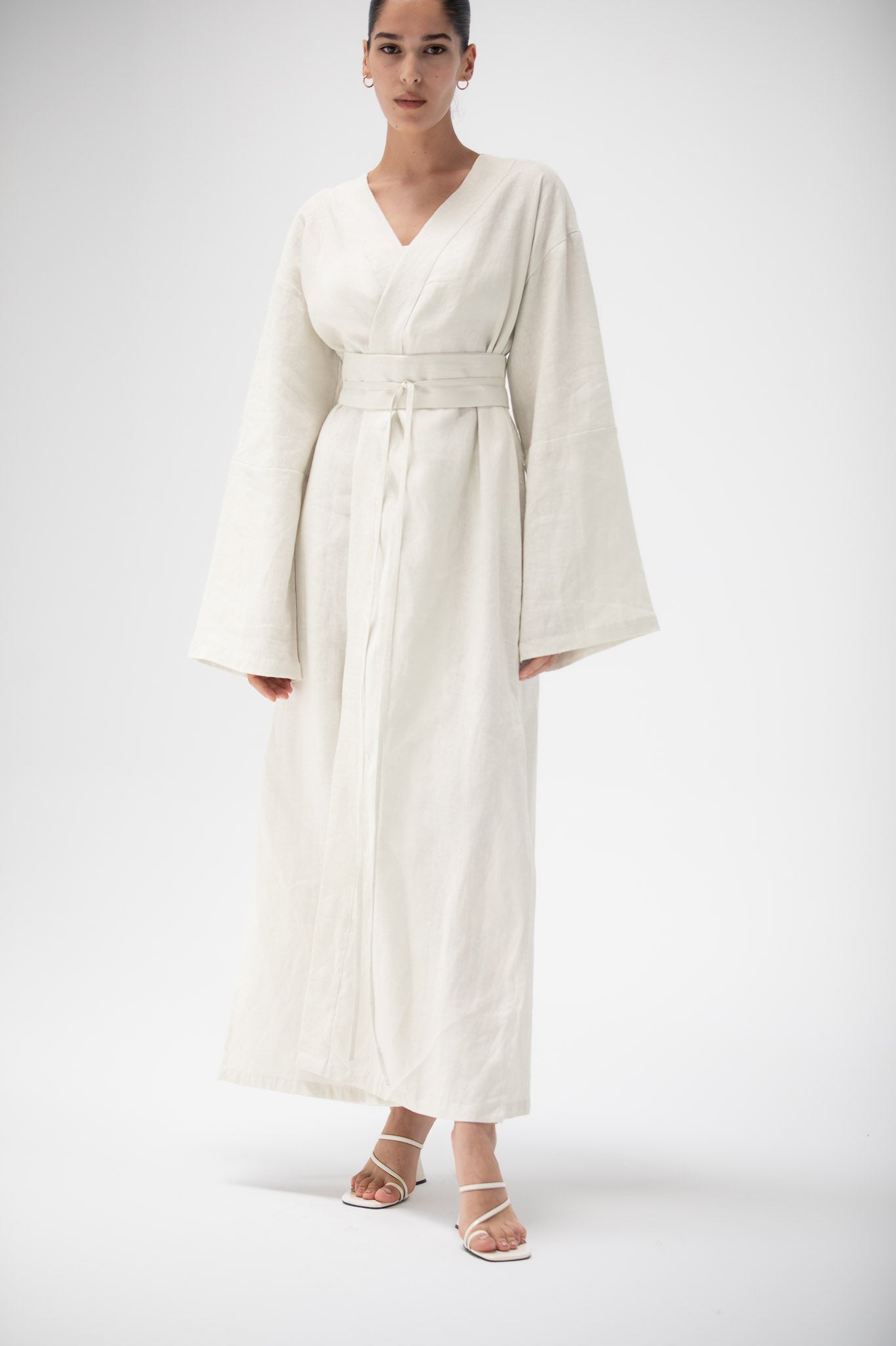 Woman wearing a linen white kimono dress with a belt on a white background.