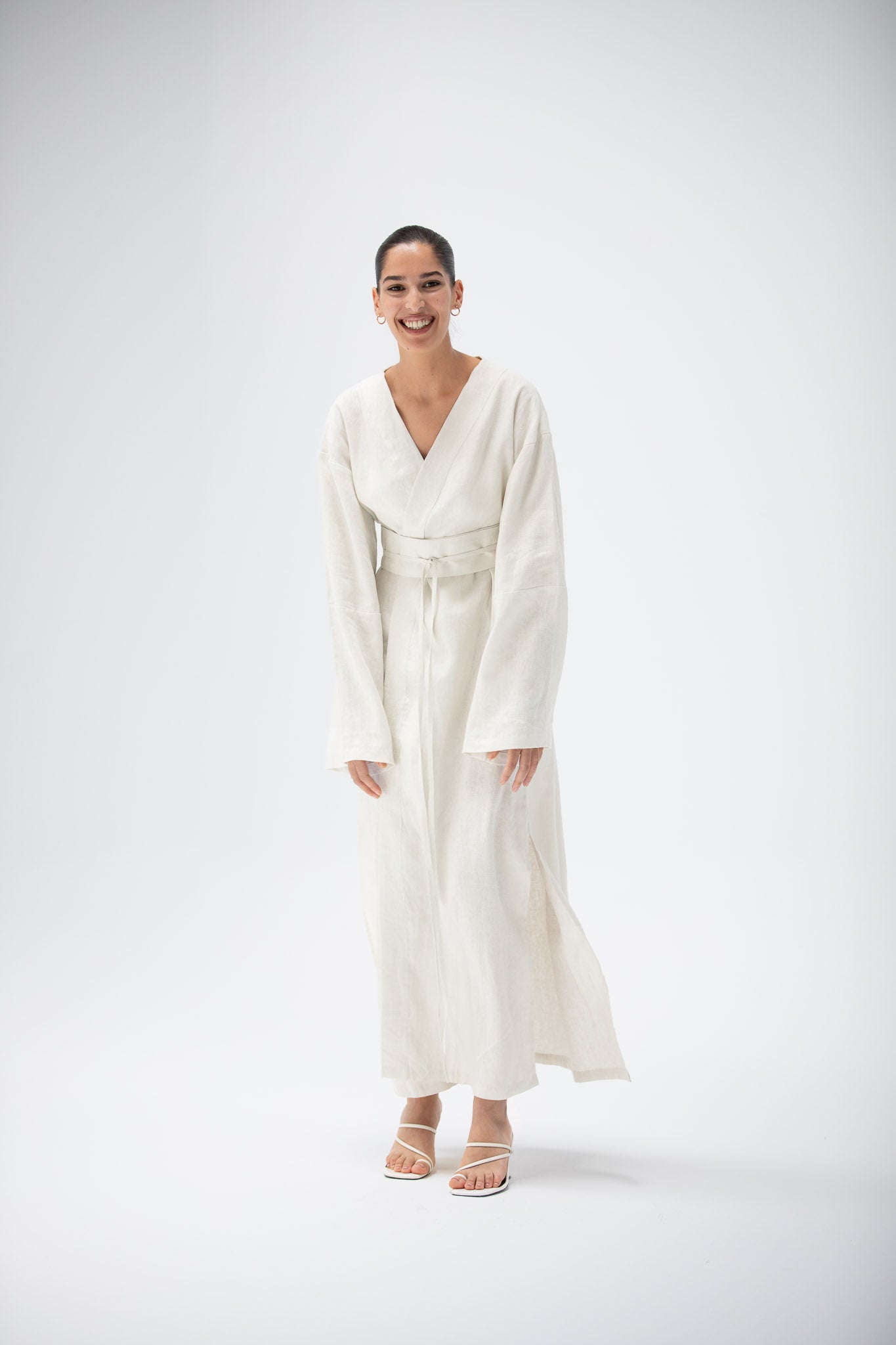 Woman wearing an ivory linen kimono dress with long sleeves on a white background