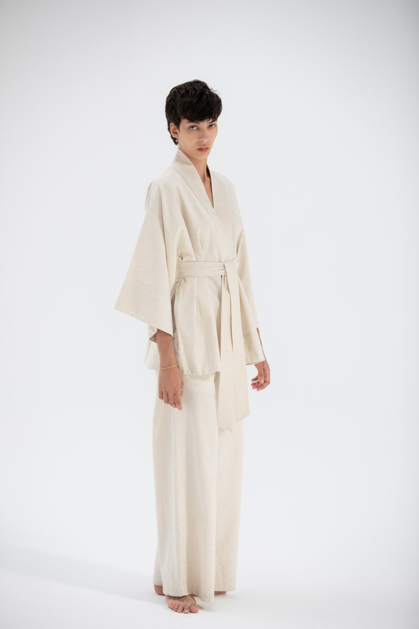 Person wearing a beige kimono jacket made of sustainable fabric.