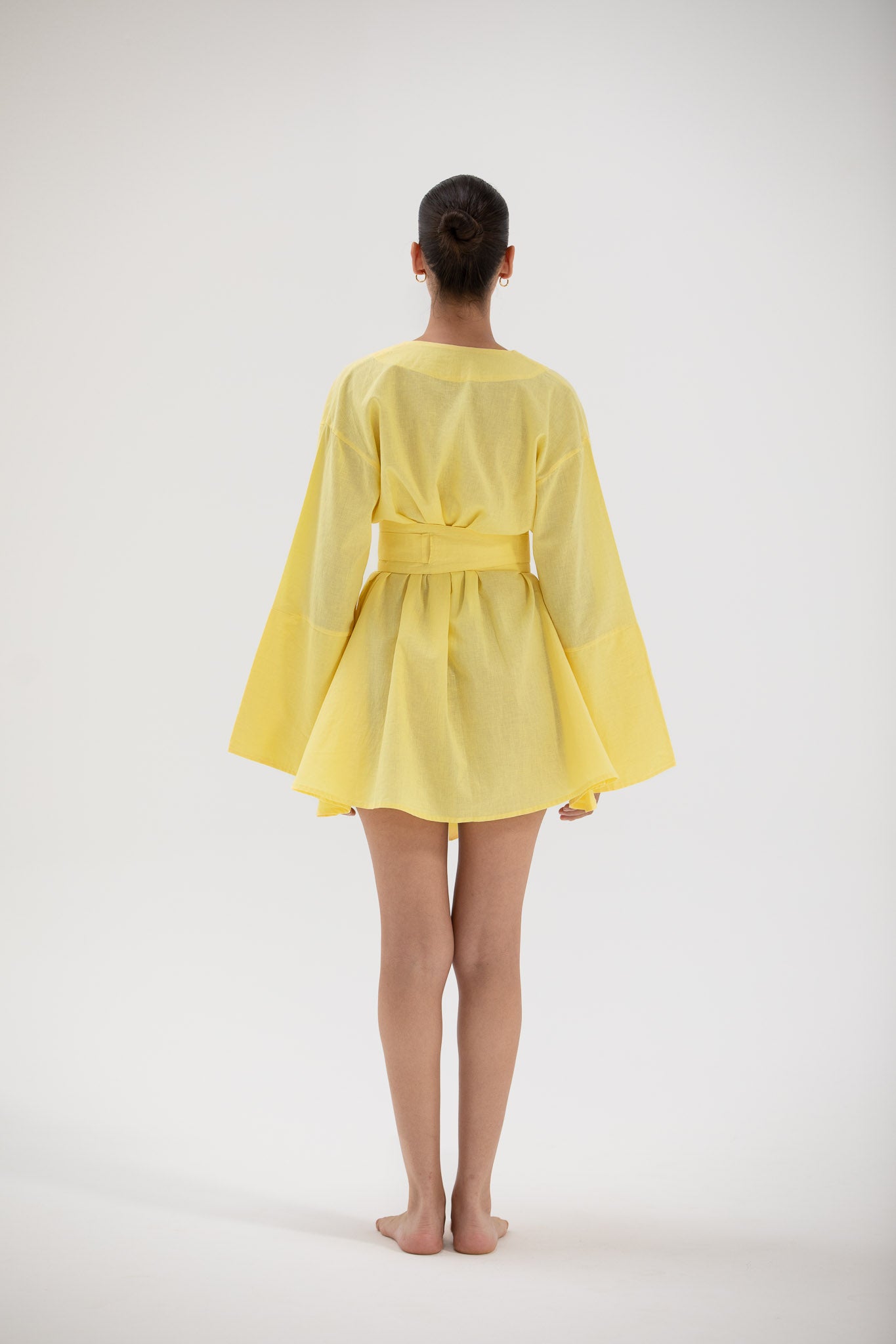 Person wearing a short yellow kimonodress with long sleeves on a white background