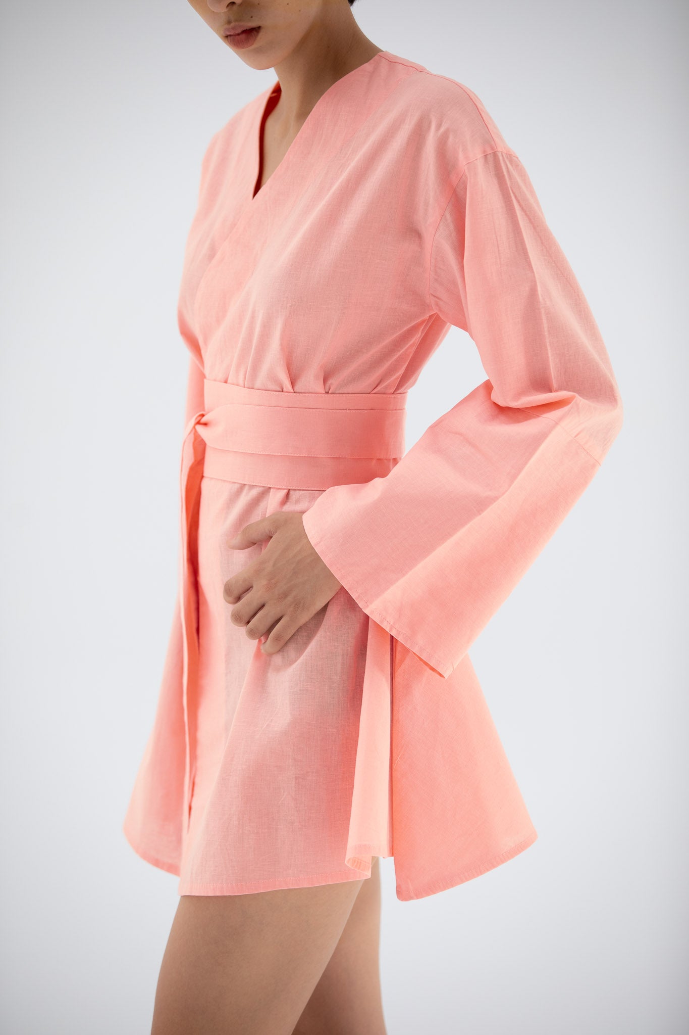 Person wearing a short pink kimono inspired dress with wild sleeves against a light gray background
