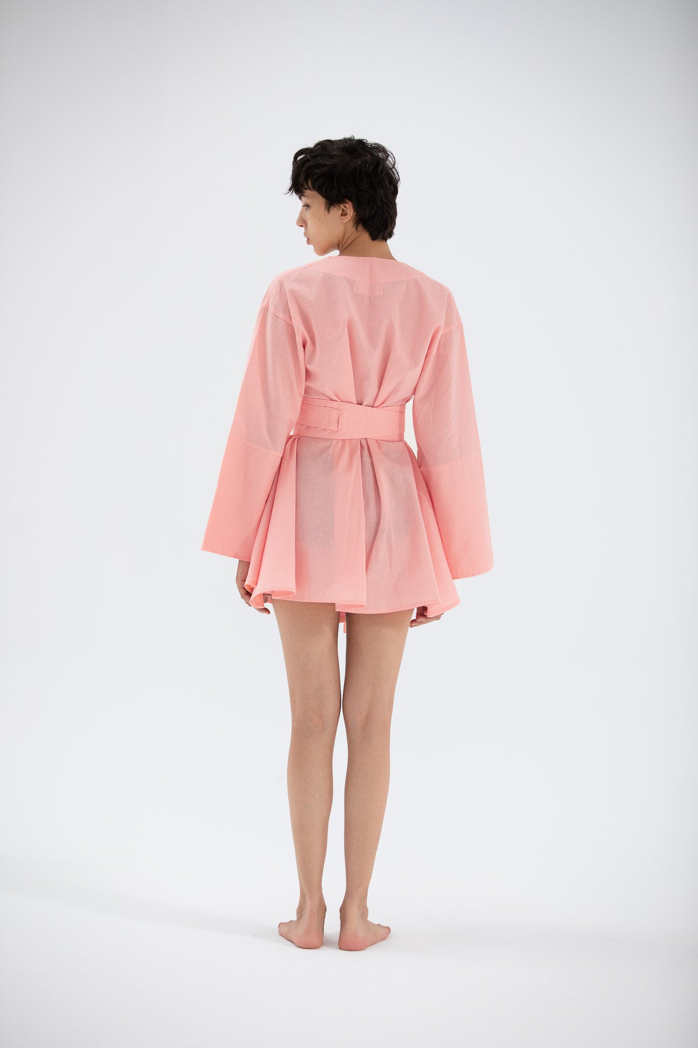 Person wearing a pink short linen kimono dress on a white background