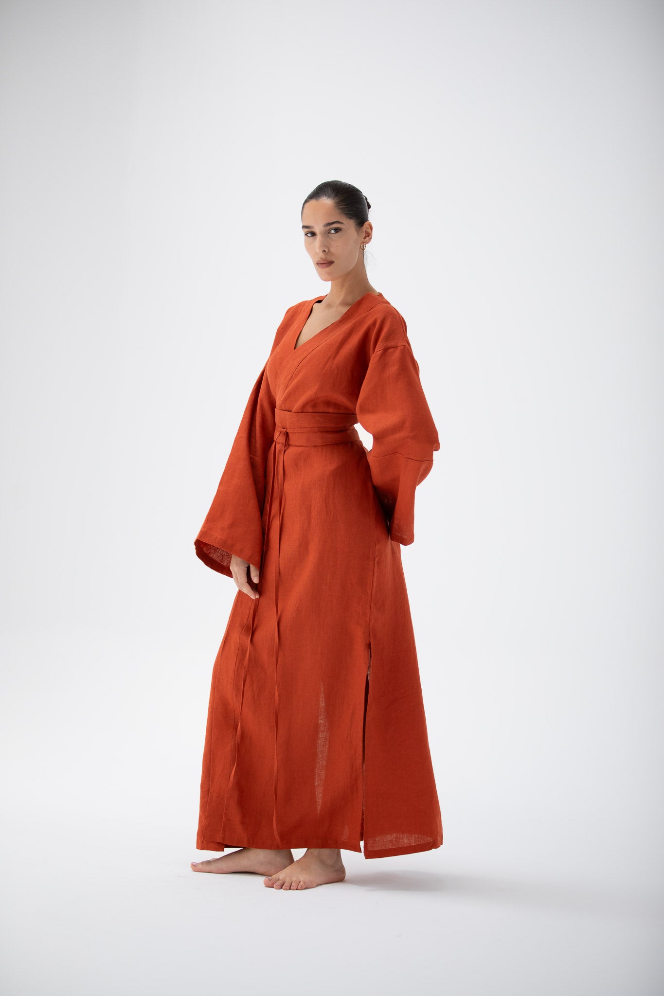 Woman wearing a terracotta kimono inspired dress designed by atelier mizuni on a white background.