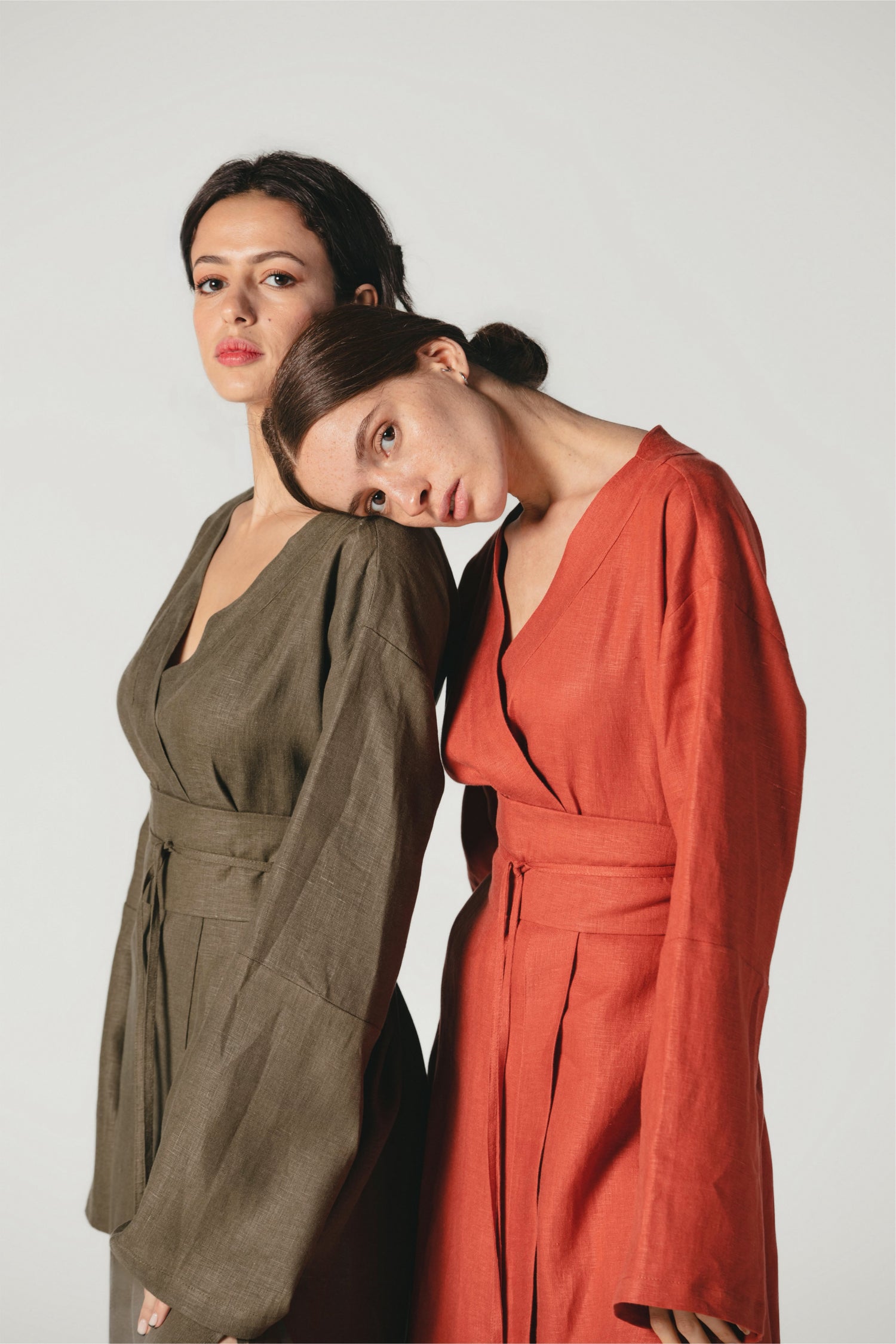 Two models showcasing our sustainable pure linen kimono dresses in dark olive green and terracotta hues. Explore sustainable fashion at Atelier Mizuni.