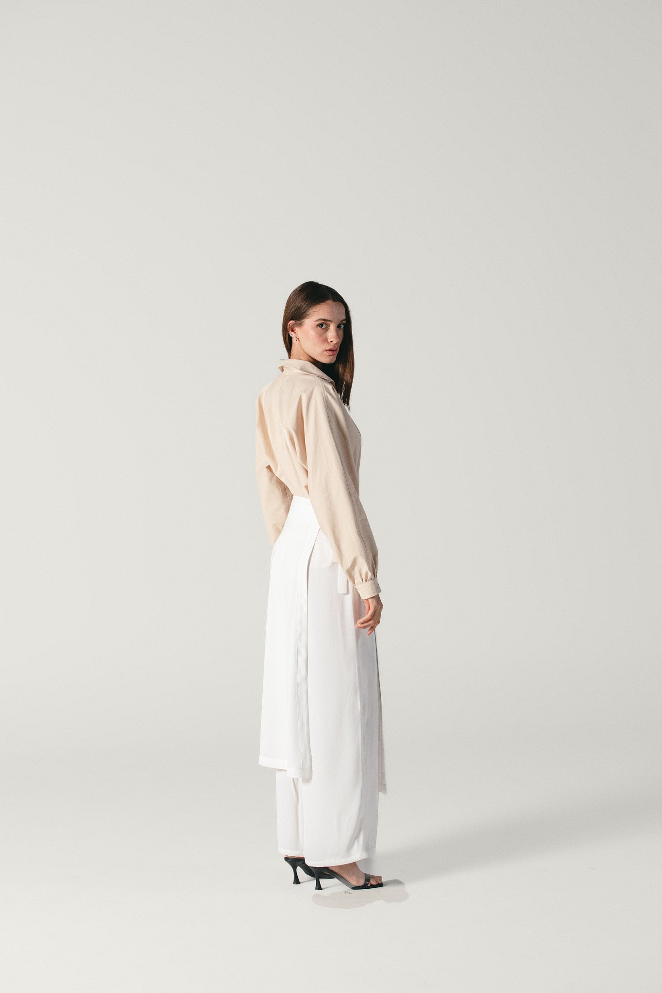 Model wearing viscose white pants with attachable skirt by Atelier Mizuni posing on the side 